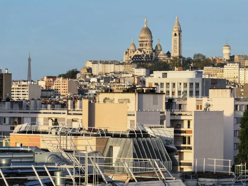 Prise de vue aérienne par drone des toits de Paris à l'heure dorée, avec le Sacré-Cœur et la tour Eiffel en arrière-plan — production audiovisuelle Dronexperts