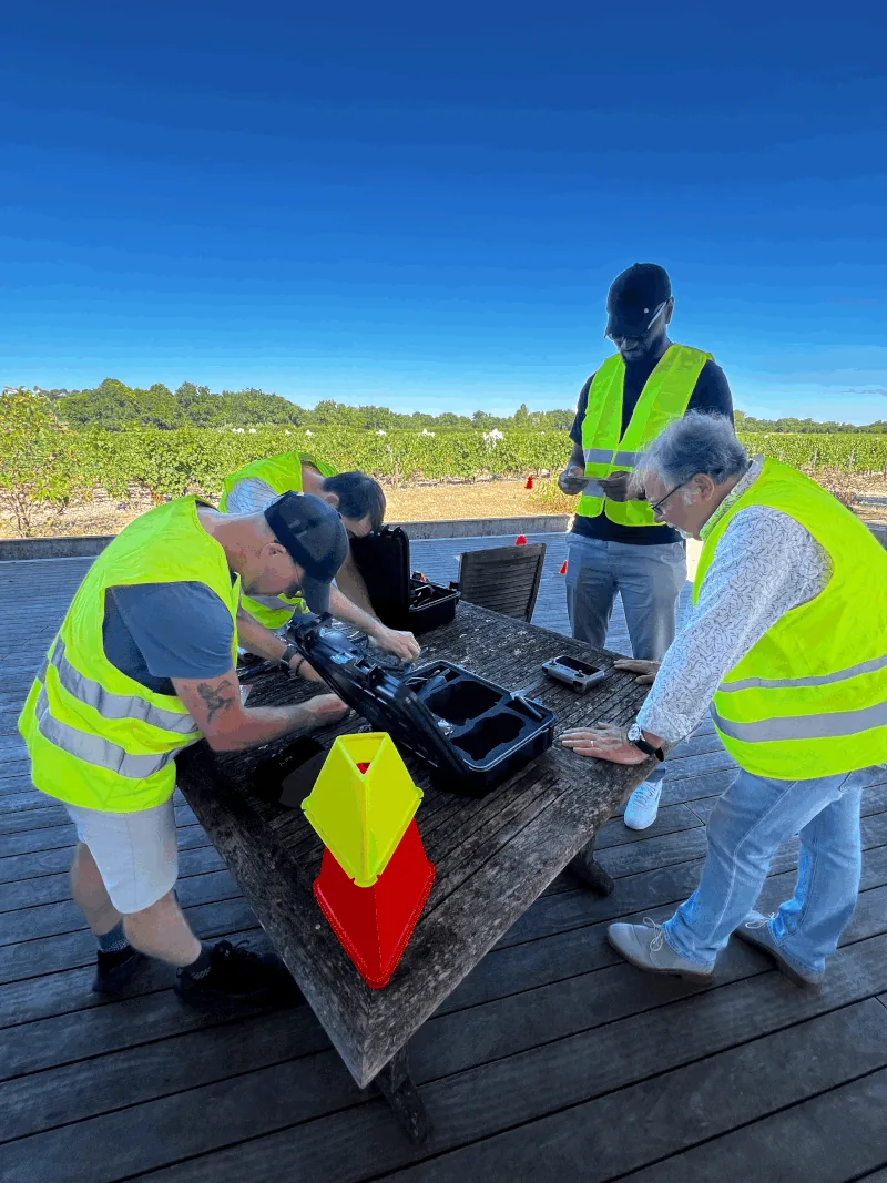 Stagiaires en gilets haute visibilité assemblant un drone sur une table lors de la session pratique en extérieur — formation de télépilote Dronexperts