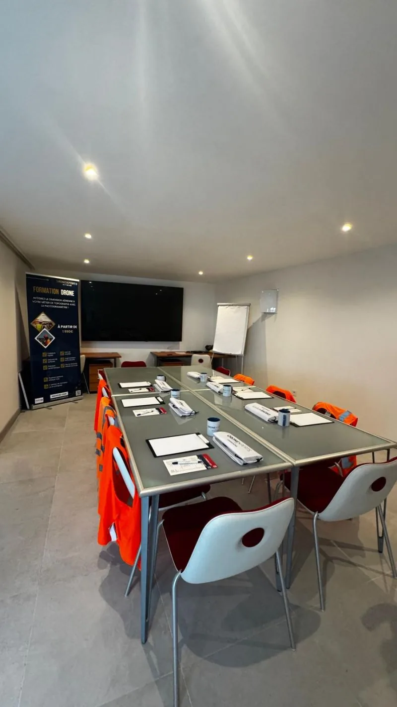 Salle de formation Dronexperts équipée pour la formation de télépilote de drone : tables, gilets haute visibilité, écran et kakémono Formation Drone