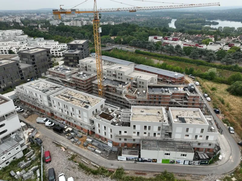 Suivi de chantier par drone — vue aérienne d'un ensemble de bâtiments résidentiels en cours de construction autour d'une grue, la Seine en arrière-plan, Dronexperts